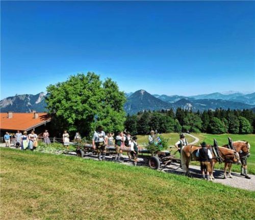 Die festliche Prozession mit dem geschmückten Weisertwecken, gezogen von vier Haflinger-Pferden, auf dem Weg zur Hohen Asten. Begleitet wird der Wagen von Personen in traditioneller bayerischer Tracht durch die malerische Berglandschaft. Petra Huber