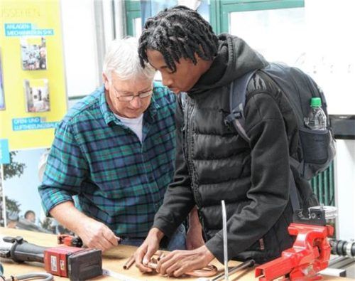 Ein Ausbilder zeigt einem jungen Mann die Arbeit mit Kupferrohren im SHK-Handwerk. Wittenzellner