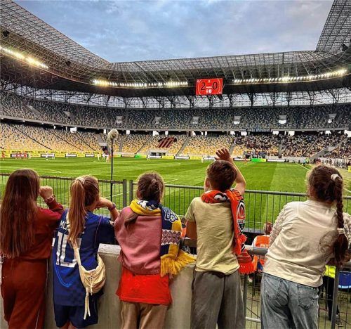 Fünf Kinder mit Fußballschals stehen am Spielfeldrand und schauen ihrem Lieblingsverein zu. Jonah Werner