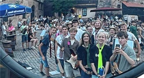 Junge Musikerinnen und Musiker der Katholischen Jugendstelle Rosenheim posieren für ein Foto, aufgenommen in einem Spiegel, während sie von einer Menschenmenge umgeben sind. Simon Dürbeck