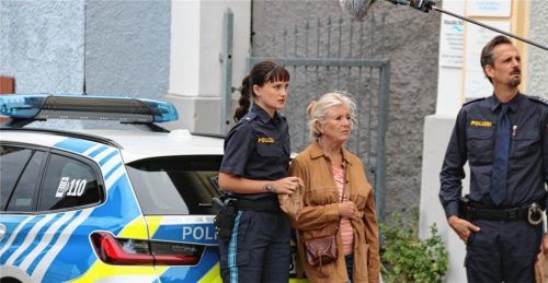 Jutta Speidel (Mitte) und Max von Thun sowie eine weitere Darstellerin stehen neben einem Polizeiauto während der Dreharbeiten in Neubeuern. Schwitteck