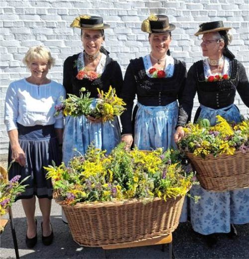 Mehrere Frauen, einige davon in Tracht, präsentieren stolz die gebundenen Kräuterbuschen in großen Körben.  Maier