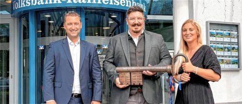 Roland Seidl, Vorsitzender der „meine Volksbank Raiffeisenbank eG“, Bastian Starflinger, Hauptgeschäftsstellenleiter in Grassau, und Annegret Daxenberger, Regionaldirektorin der Region Chiemgau, sind bei der symbolischen Schlüsselübergabe vor der Filiale in Grassau zu sehen. meine Volksbank Raiffeisenbank eG