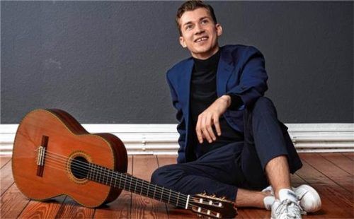 Der französische Gitarrist Thibaut Garcia sitzt entspannt mit seiner Gitarre auf dem Holzboden. Mélissa Kavanagh